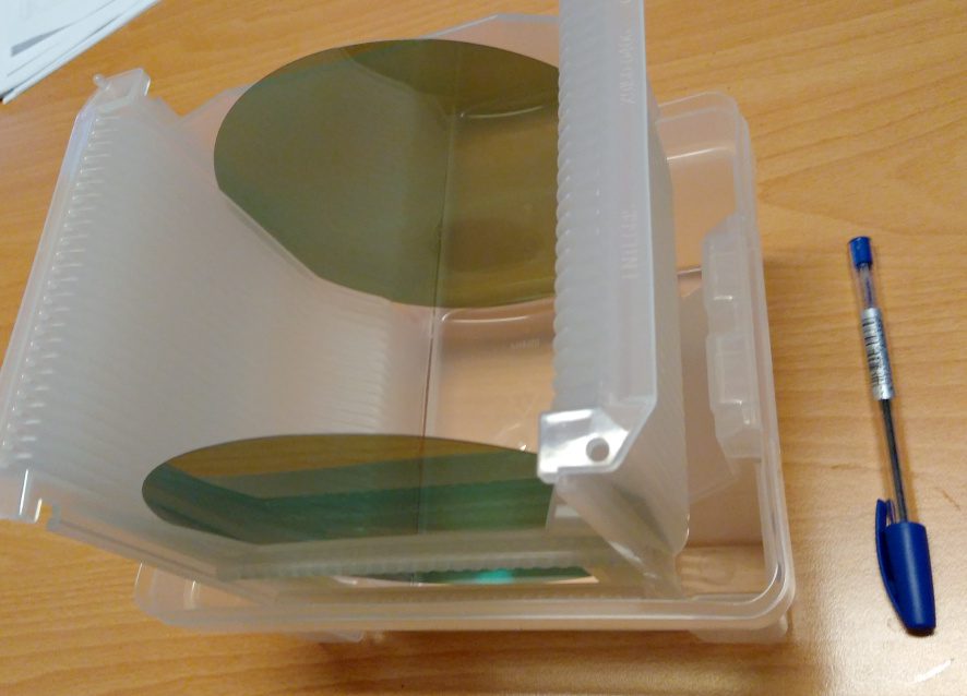 Two 6-inch silicon carbide wafers in a plastic wafer carrier next to a pen